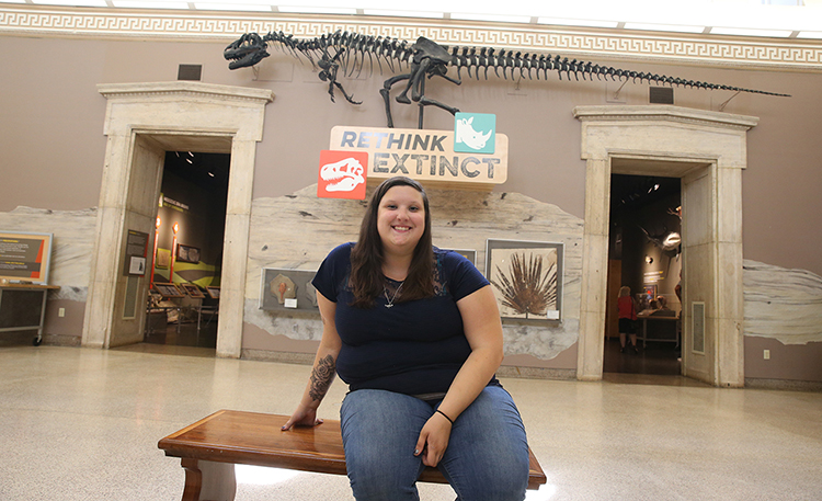 Violet Lent sitting in front of dinosaur skeleton 
