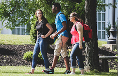 Three students walking on campus during the summer viewed from their left side