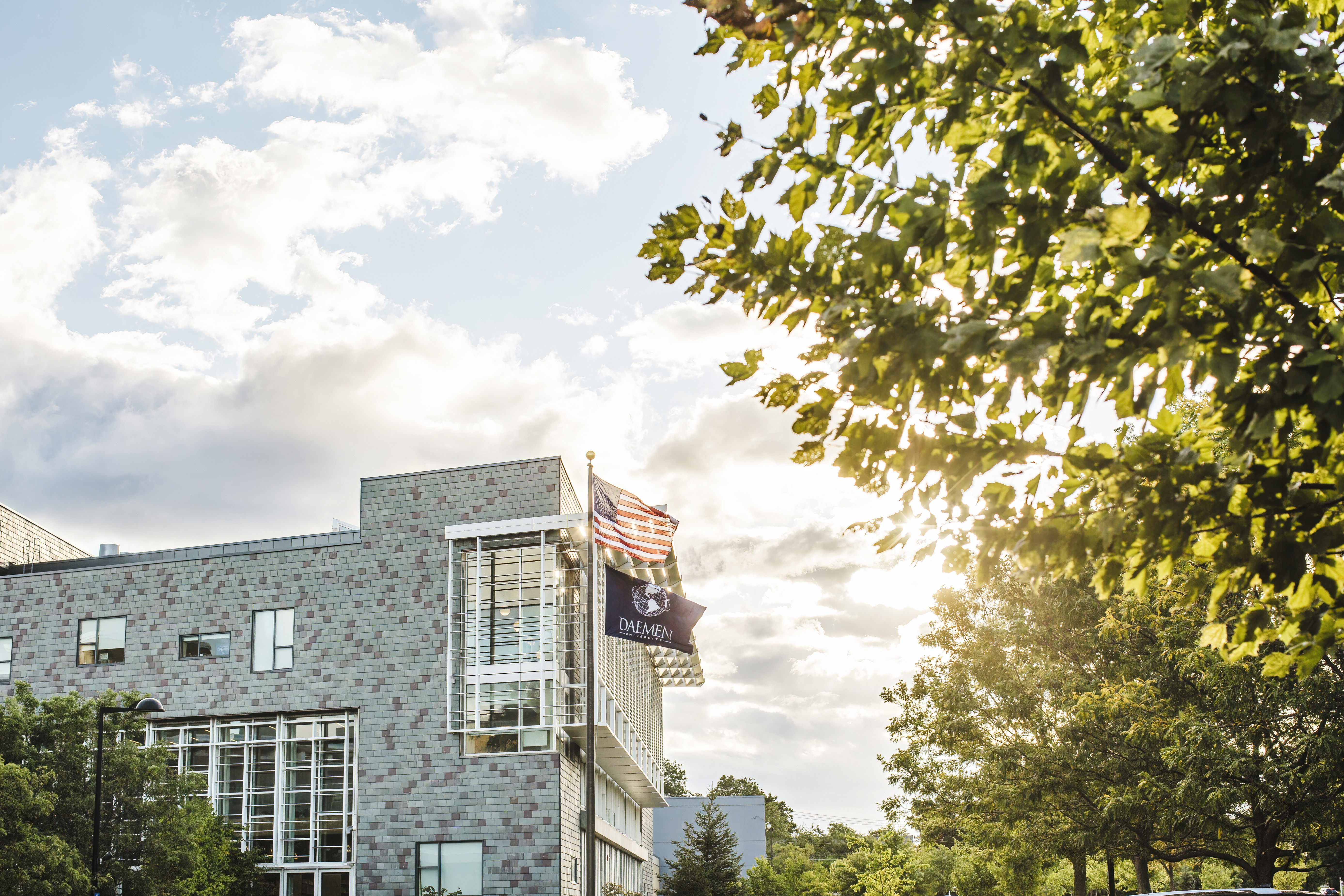 Brick building with windows and the American flag and Daemen University flag flying on a flag pole