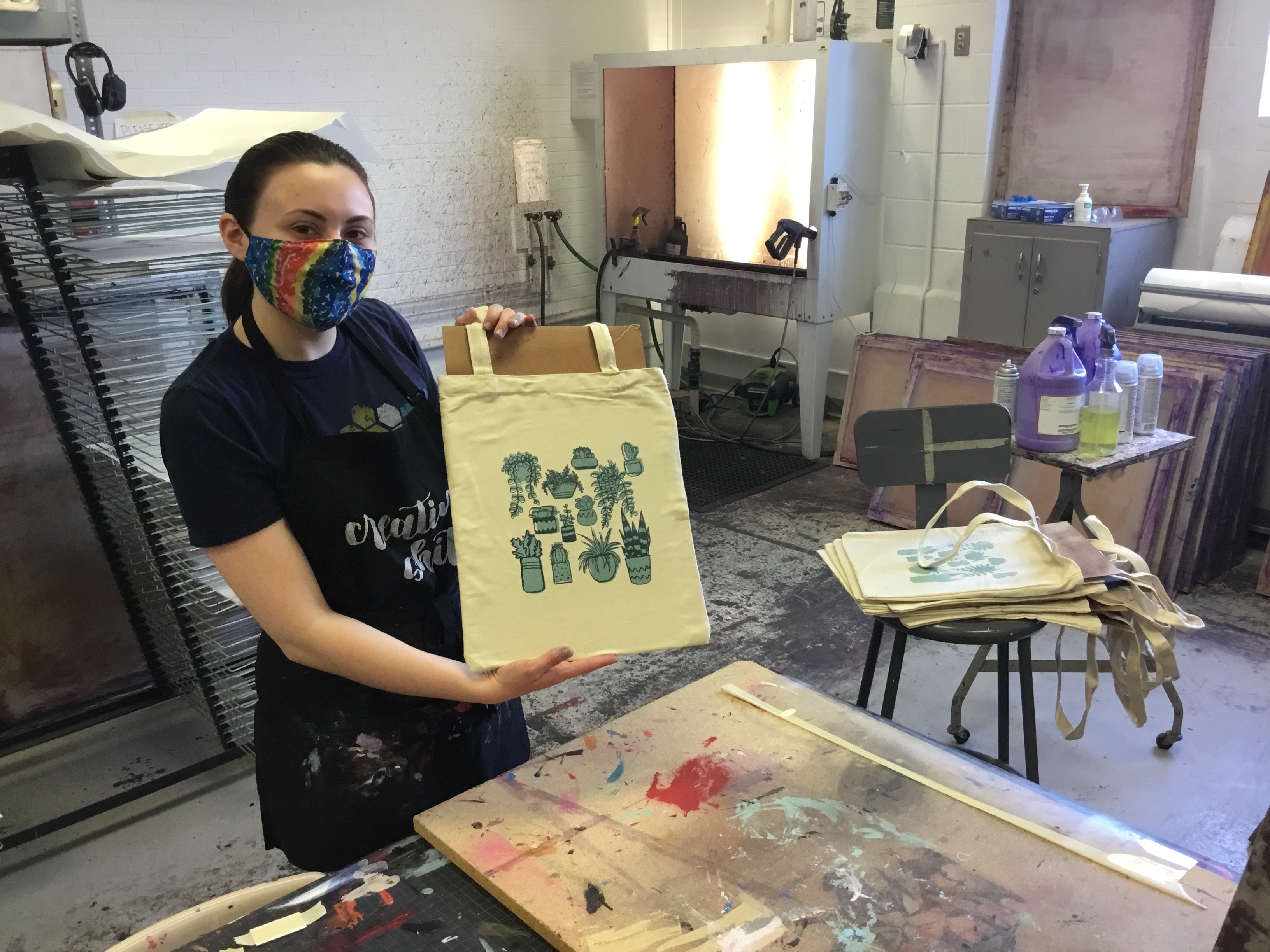 Emma Lonnen wearing a mask displaying the finished project in Serigraphy class