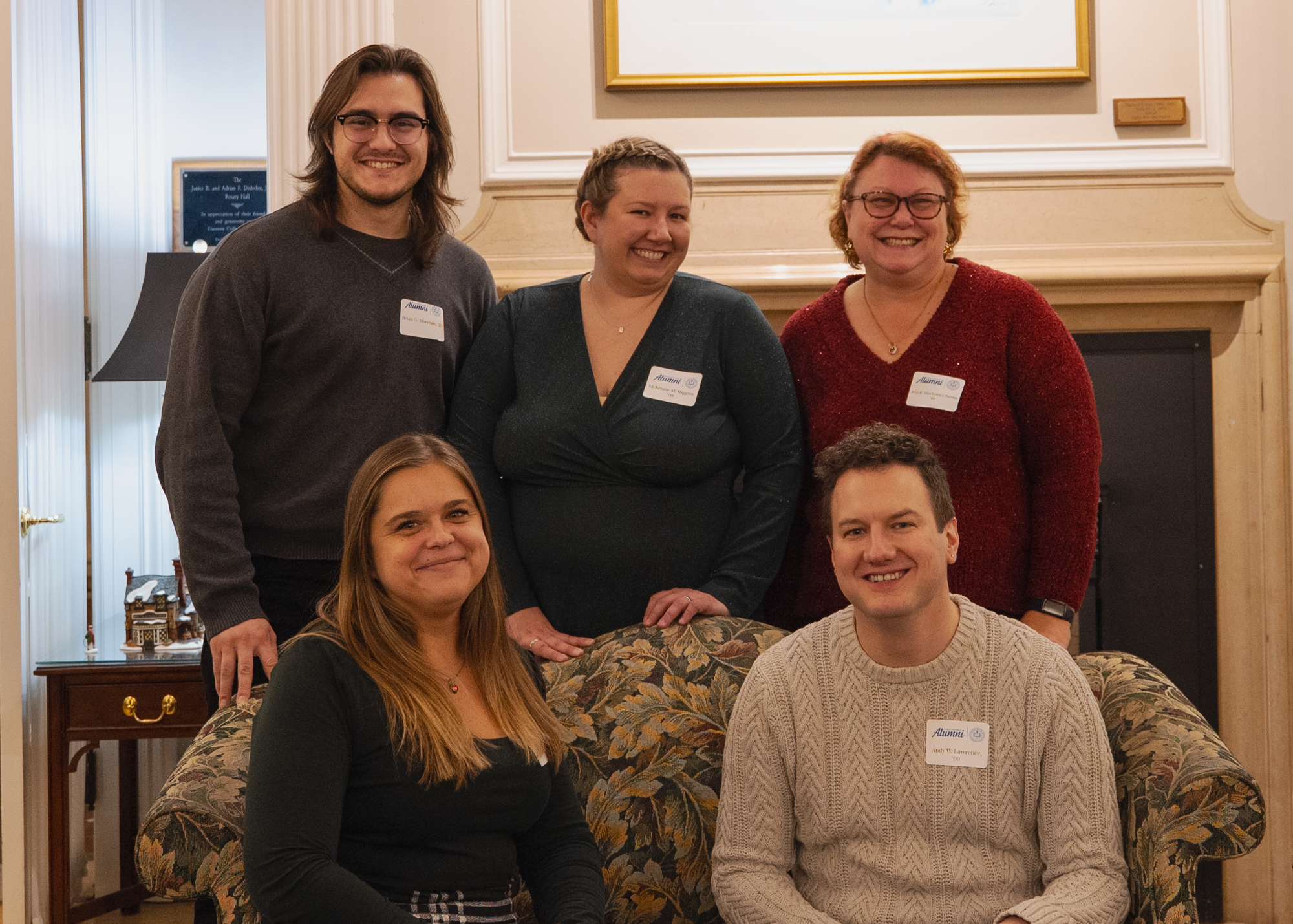 five people sit indoors by fireplace
