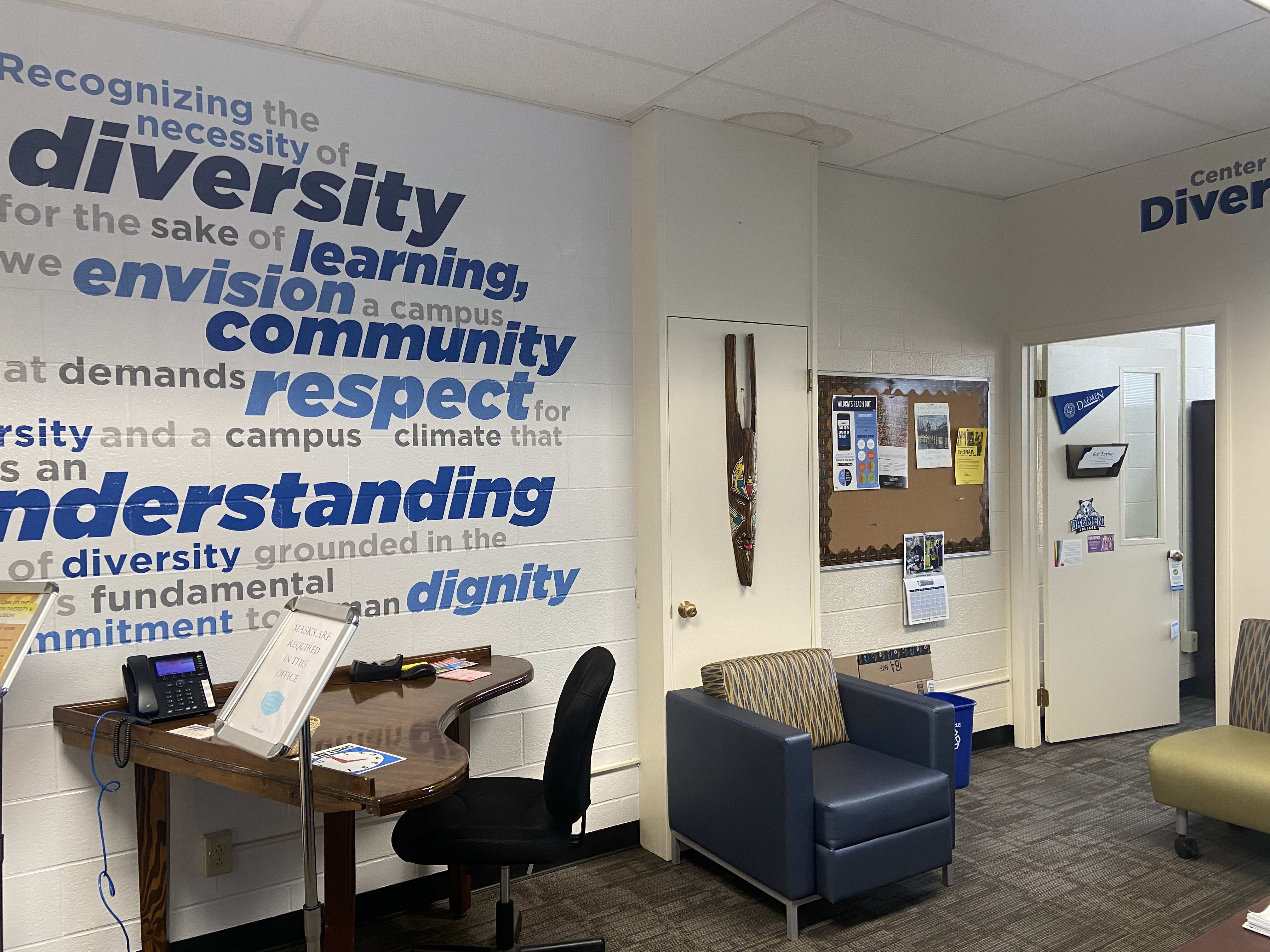 A large wall with a blue word cloud, a desk, and a lounge chair.