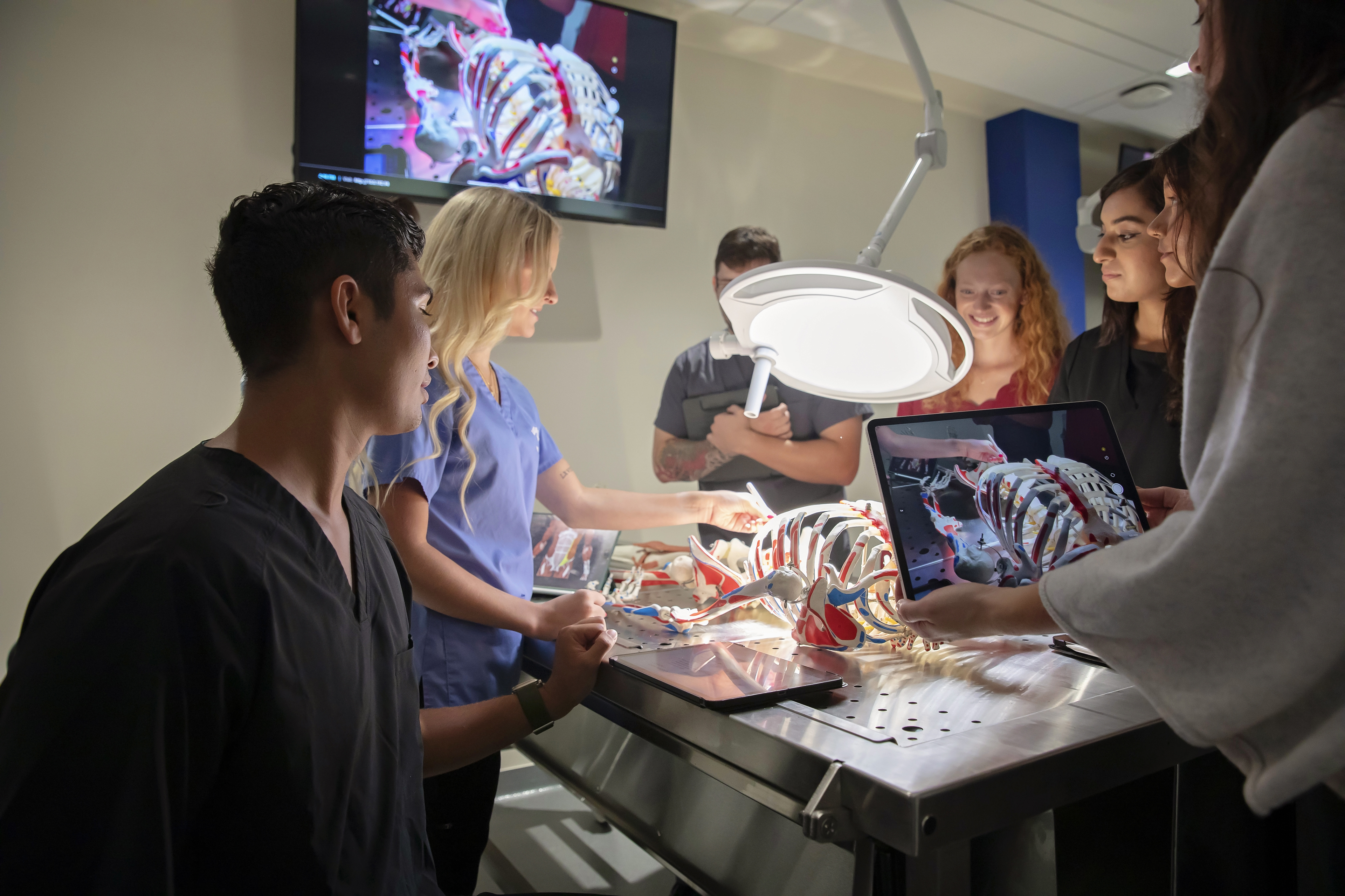 Male and female students standing around a surgical table reviewing a skeleton together