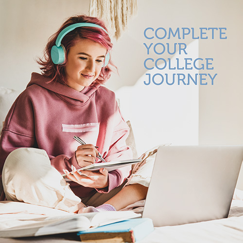 Female student in a hoodie sitting cross legged with headphones on taking notes during an online class