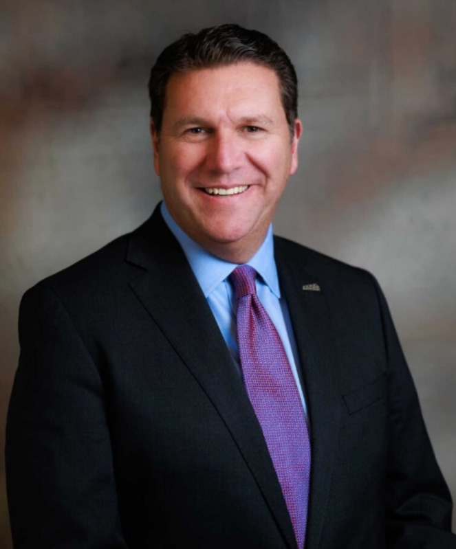 Man with short dark hair wearing a blue dress shirt, red and blue tie and dark sport coat