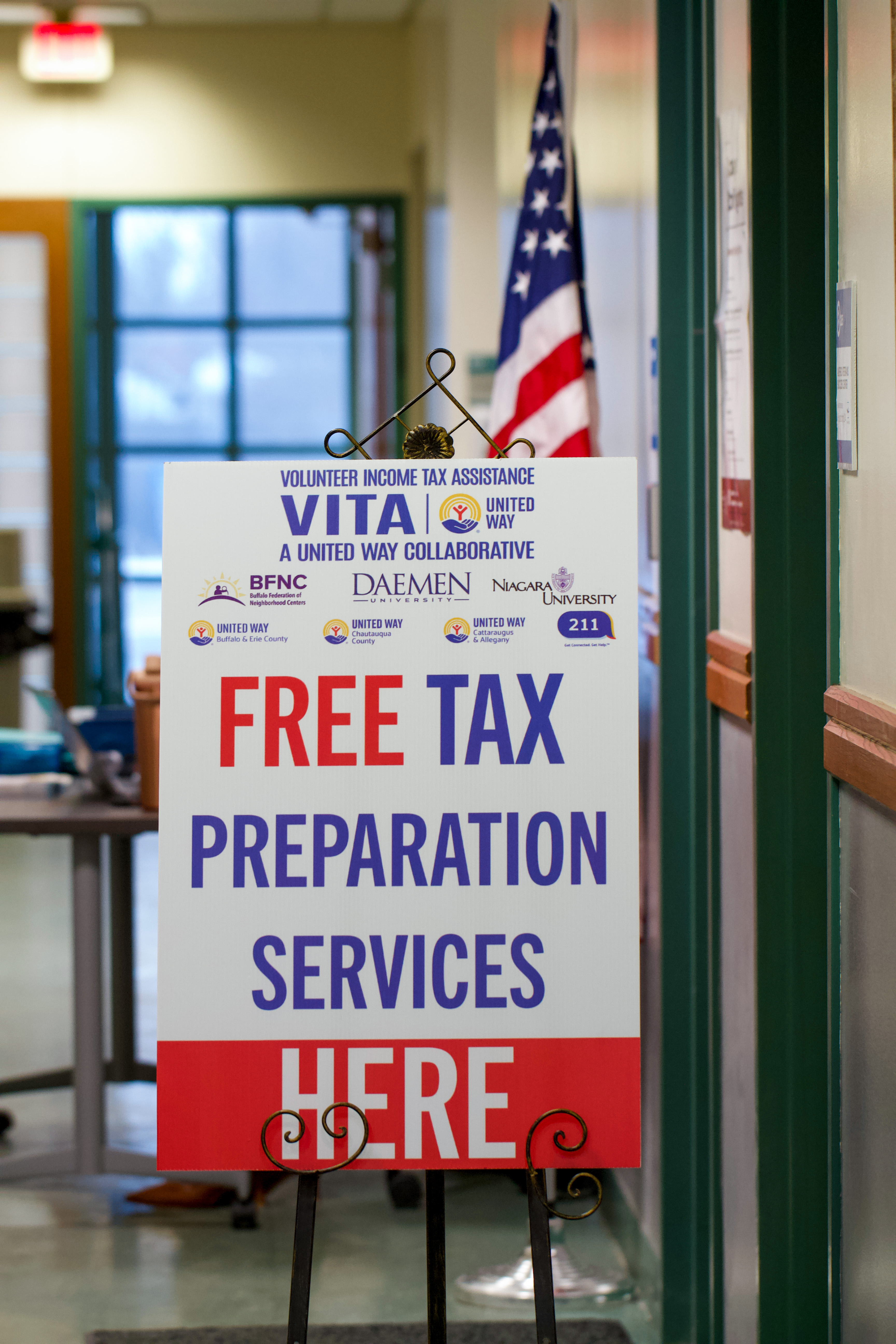 White sign with red and blue letters on an easel in front of an American flag