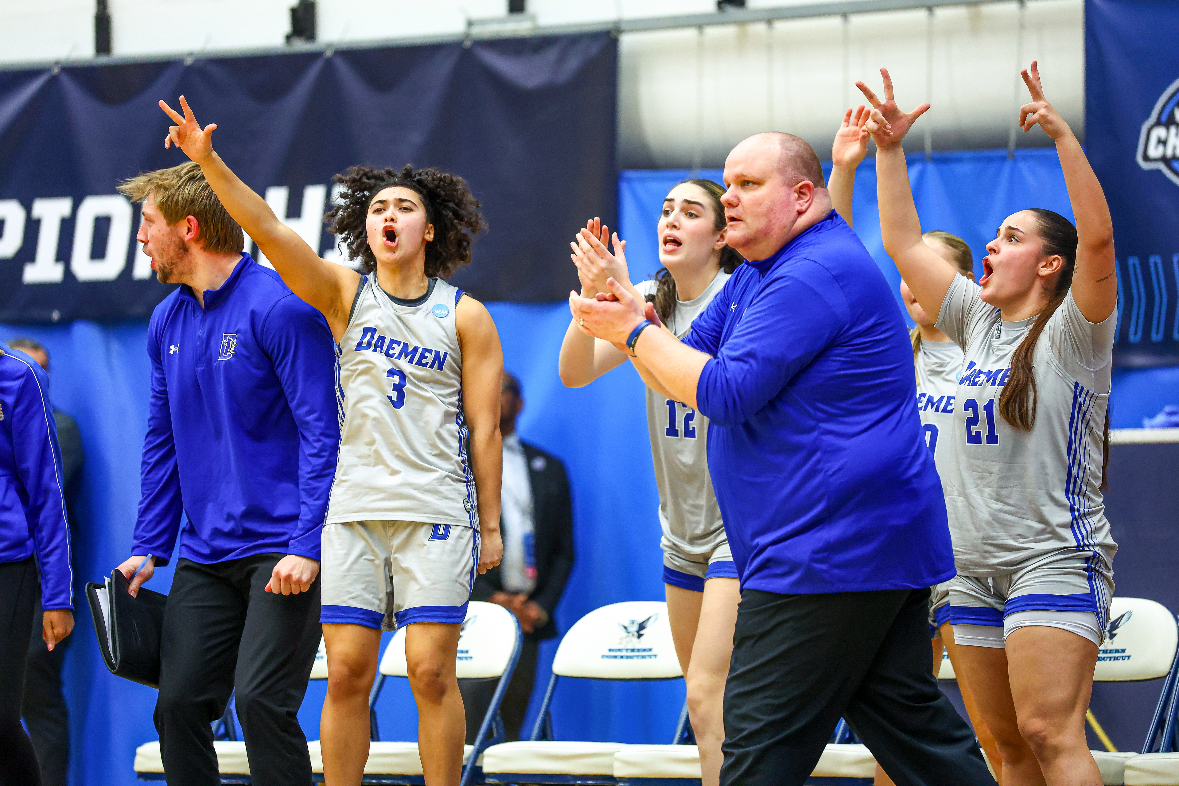 Women's college basketball players standing on the side of the court while the coach claps and walks past them