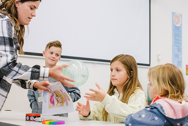 Therapist working with three sitting children, passing them a ball