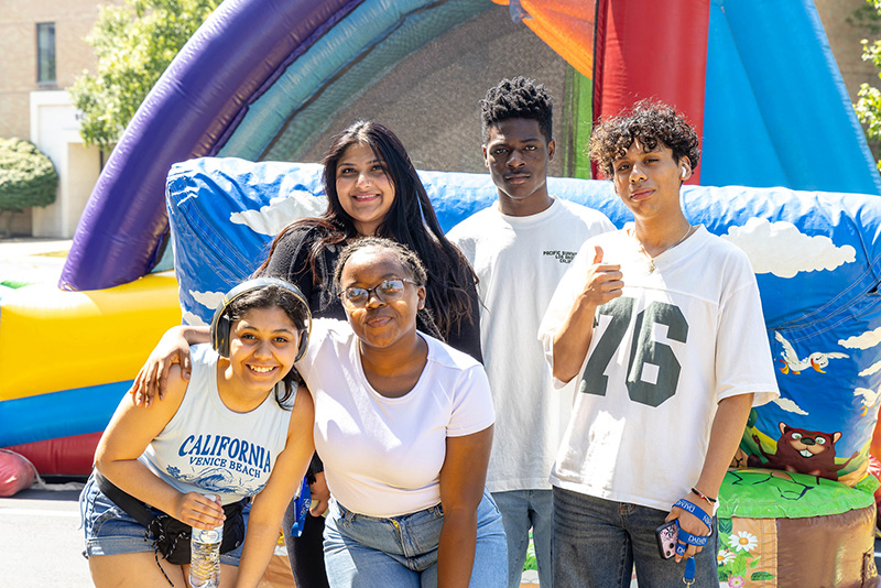 Five students at Daemen Bock Party, inflatable rainbow bounce house behind them