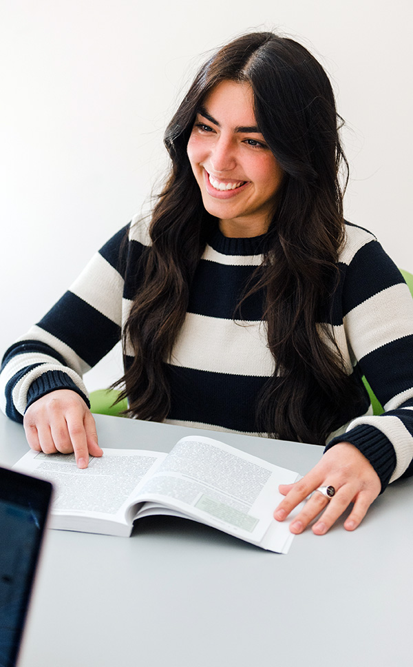 Female student sitting at a table holding a book smiling