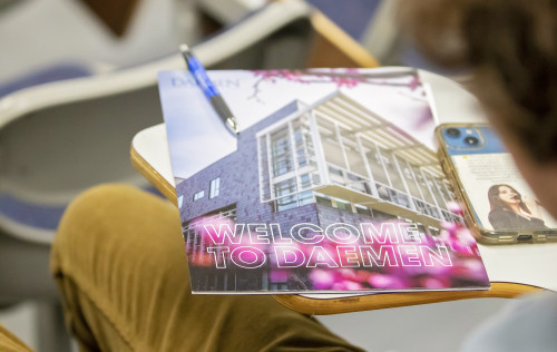Welcome to Daemen orientation book on a desk a student is sitting at