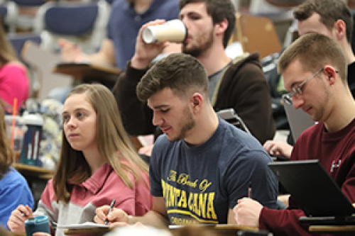 Students sitting in a stadium seating class taking notes