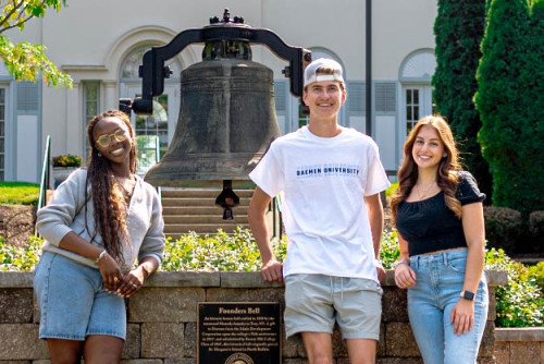 Three Daemen students posing for a photo in front of Founders Bell on the Daemen campus.