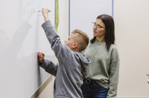 Therapist working with student who is writing on a white erase board