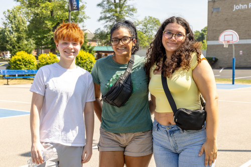 three students standing on the outdoor basketball court