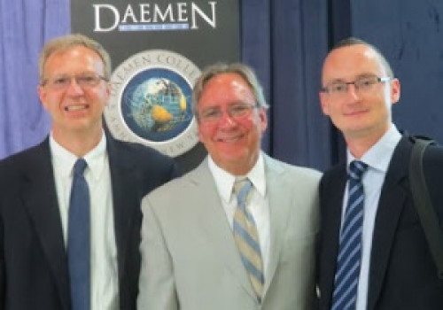 Three men in suites standing in front of Daemen podium 