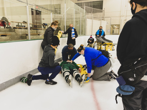 Athletic Training staff helping hockey player laying on the ice