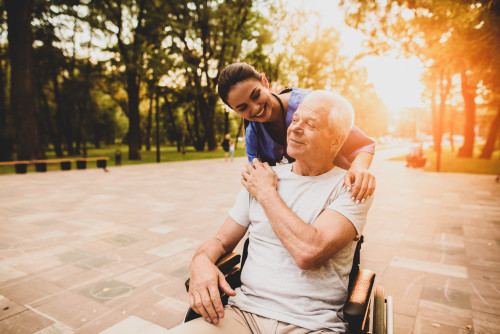 Nurse and elderly patient in a wheelchair outside at sunset 