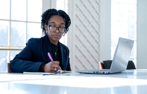 grad student sitting at table in rosary hall sun room with laptop