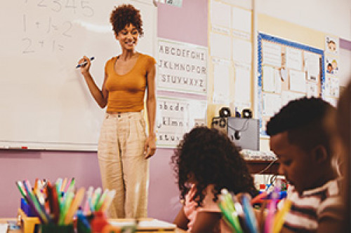 Female teacher standing in front of a white board teaching match to grade school kids