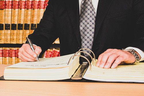 Lawyer in suit at desk writing in book with rows of legal books behind them