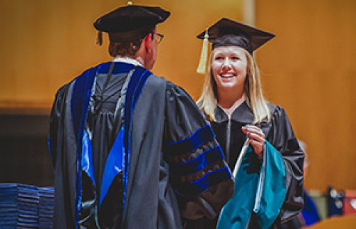 Female student shaking hands with President Olson as they walk across the stage at Kleinhanns Music Hall during commencement