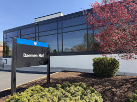 The exterior of a large building with glass windows and a dark sign out front with white letters