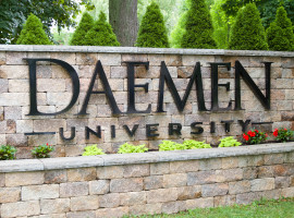 Daemen University sign on a stone wall with flowers, plants and trees around it