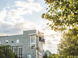 Brick building with windows and the American flag and Daemen University flag flying on a flag pole
