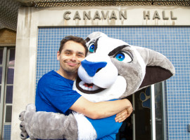 Man hugging Daemen's Willie mascot in front of Canavan Hall