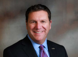 Man with short dark hair wearing a blue dress shirt, red and blue tie and dark sport coat