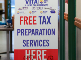 White sign with red and blue letters on an easel in front of an American flag