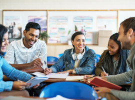 Five college students sitting at a table interacting with each other
