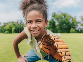 Adolescent girl holding a softball mitt playing in a field